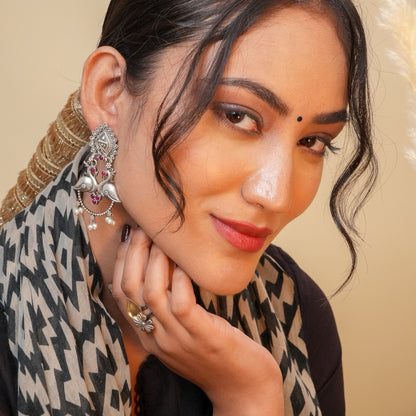 Woman wearing intricate earrings and a patterned scarf against a beige background