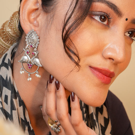 Close-up of a woman wearing a silver earring with red stones on a beige background